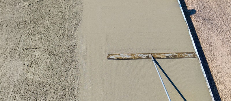 a fresh pad of poured concrete being smoothed by a large rake