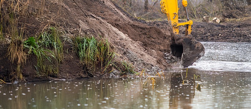 a pond with an excavator on the banks scooping out the sides to maintain it